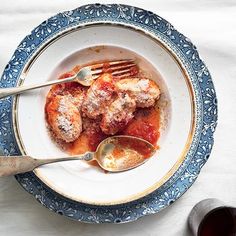 a white plate topped with meat covered in sauce next to a glass of red wine