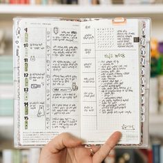 a person holding up a notebook with writing on it in front of a bookshelf