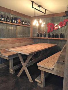 a wooden table and benches in a room with bottles on the wall behind it,