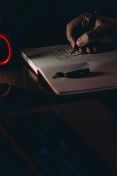 a person writing on a notebook with a red light in the dark next to them