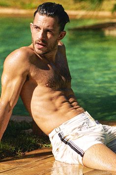 a shirtless man laying on the ground next to a body of water