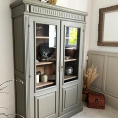 a cabinet with glass doors and shelves in a living room next to a vase on the floor