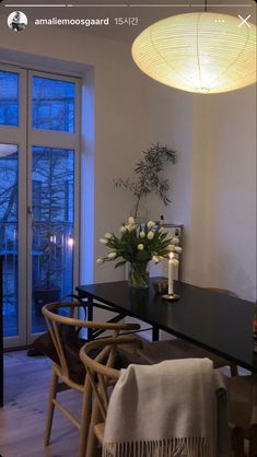 a dining room table and chairs with flowers in the vase next to it, near a large window