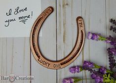 a wooden horseshoe with the words lucky one on it next to purple flowers and a note