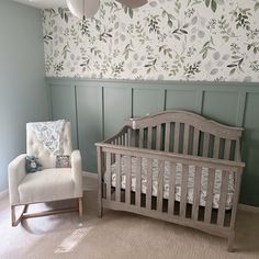 a baby's room with a crib, chair and wallpaper