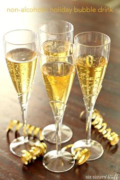 three glasses filled with champagne sitting on top of a wooden table next to gold decorations