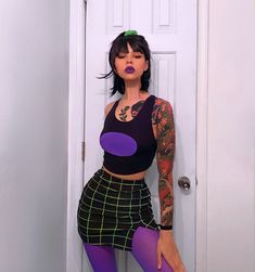 a woman with tattoos and purple tights posing in front of a white door,