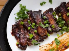 some meat is on a plate with green onions and cilantro sprigs