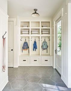 an entry way with white cabinets and gray tile flooring, two coats hanging on hooks