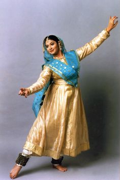 a woman in a gold dress and blue shawl is posing for the camera with her arms outstretched