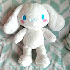 a white stuffed animal with blue eyes sitting on a green and white checkered blanket