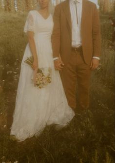 a man and woman standing next to each other in a field with trees behind them