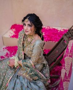 a woman in a blue and gold wedding dress sitting on the ground next to pink flowers