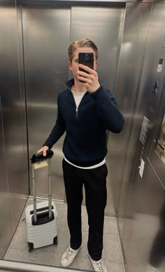 a man taking a selfie in front of an elevator with his suitcase and cell phone