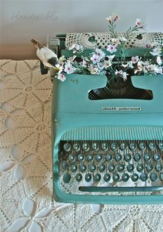 an old - fashioned typewriter with flowers on the top, sitting on a doily