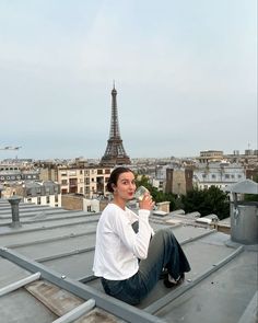 a woman sitting on top of a metal roof drinking from a glass in front of the eiffel tower