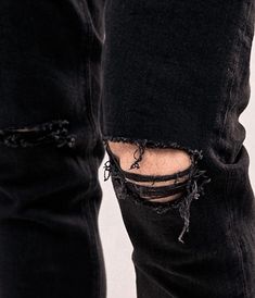 a pair of black ripped jeans with holes on the legs and knees, both worn by someone