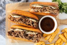 three sandwiches with meat, cheese and french fries on a cutting board next to dipping sauce