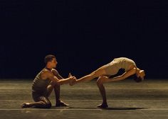 two dancers performing on the floor in front of a black background, one is doing a handstand