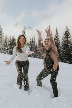 two people are playing in the snow with their hands up and one person is wearing black pants