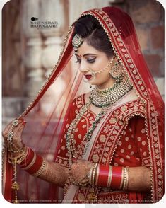 a woman in a red and gold bridal outfit is looking down at her jewelry