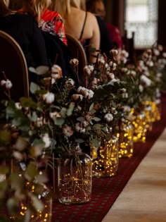 flowers in vases lined up on a long table with people sitting at the end