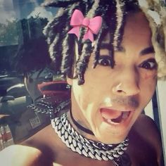 a man with dreadlocks and a pink bow on his head is making a funny face