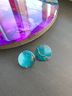 two blue and gold earrings sitting on top of a table next to a purple mirror