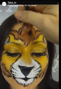 a woman is getting her face painted yellow and white with a tiger's head