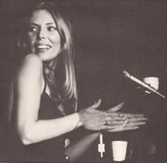 a black and white photo of a woman sitting at a table in front of a microphone