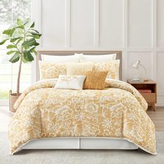 a bed with yellow and white comforters in a room next to a plant on the floor