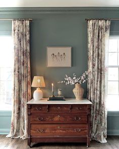 a dresser with two vases on top of it next to a window covered in curtains