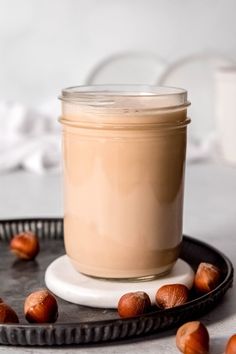 a glass jar filled with liquid sitting on top of a pan covered in nuts next to a cup of coffee