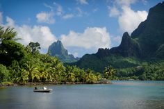 a small boat floating on top of a lake surrounded by lush green mountains and palm trees