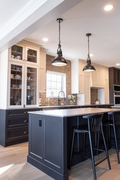 a large kitchen with an island in the middle and two hanging lights on the ceiling