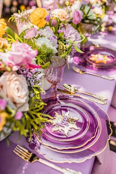 the table is set with purple and yellow plates, silverware, and floral centerpieces