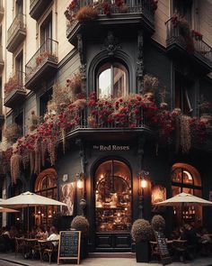 an old building with flowers growing on the side and tables in front, along with umbrellas