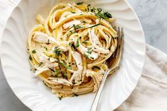 a white bowl filled with pasta covered in chicken and parsley next to a fork