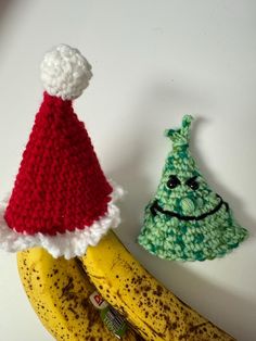 two crocheted christmas hats sitting on top of bananas