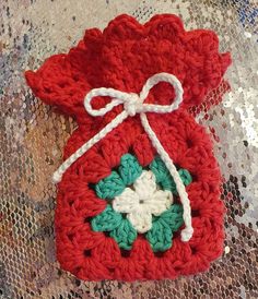 a crocheted red bag with white and green flowers on the front sits on a table