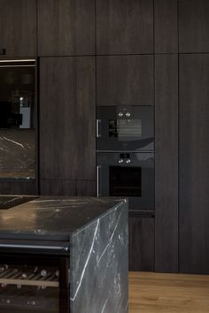 a kitchen with marble counter tops and black appliances in the backround, along with dark wood paneling