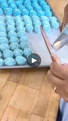 a person is using scissors to cut cupcakes with blue frosting on them