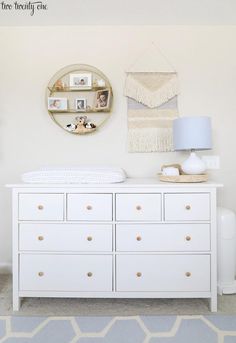 a baby's room with a white dresser and wall hangings on the wall