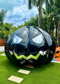 a large black pumpkin shaped object sitting on top of a lush green field next to palm trees