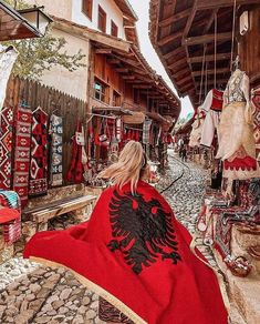 the woman is walking down the cobblestone street with her red and black shawl