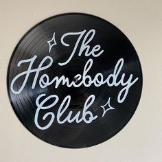 a black record with the words the somebody club on it hanging from a white wall