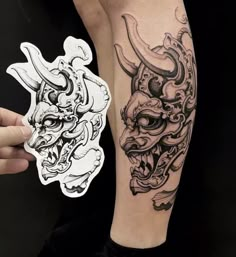 a person with a tattoo on their arm holding up a sticker that has an image of a demon