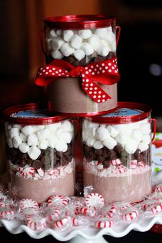 three jars filled with candy and marshmallows on top of a cake plate