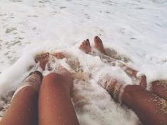 two people laying on the beach with their feet in the water