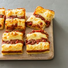 several square slices of lasagna on a wooden cutting board with cheese and sauce